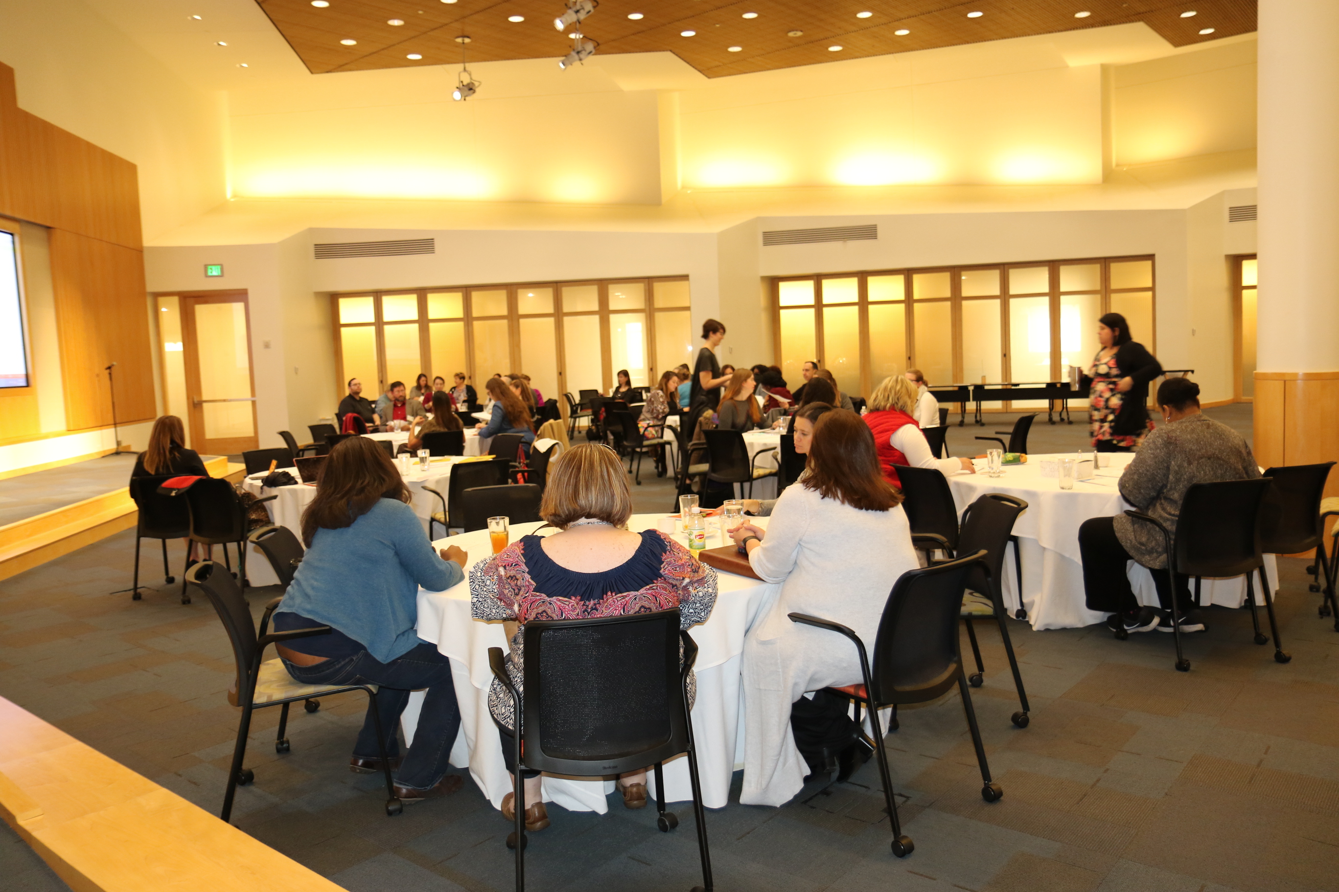 Photo: View of the back of the room, with all of the attendees visiting at tables at the November 2017 Family to Family Stakeholder's Meeting